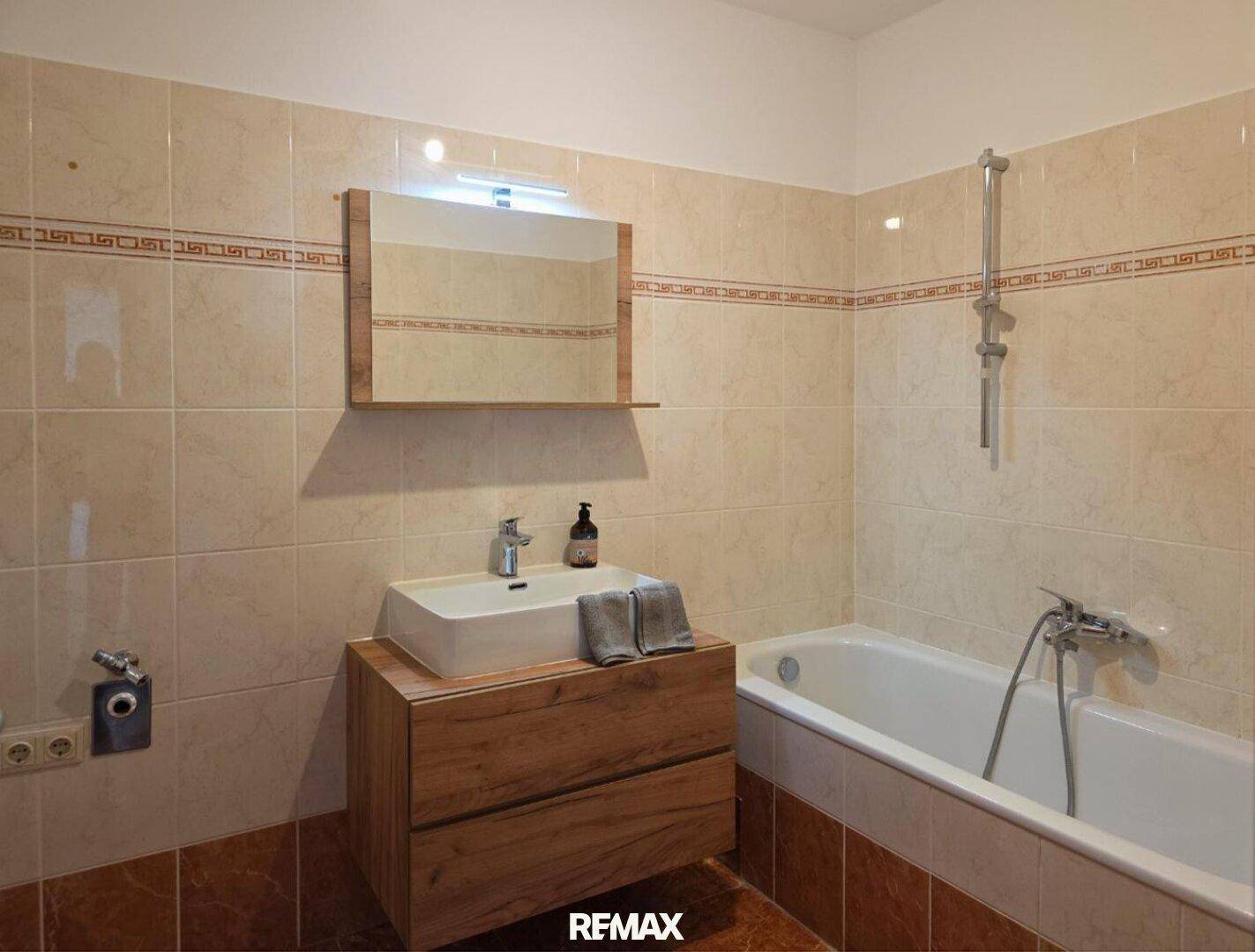 Gefliestes Badezimmer mit Badewanne, modernem Waschbecken und Holzunterschrank.