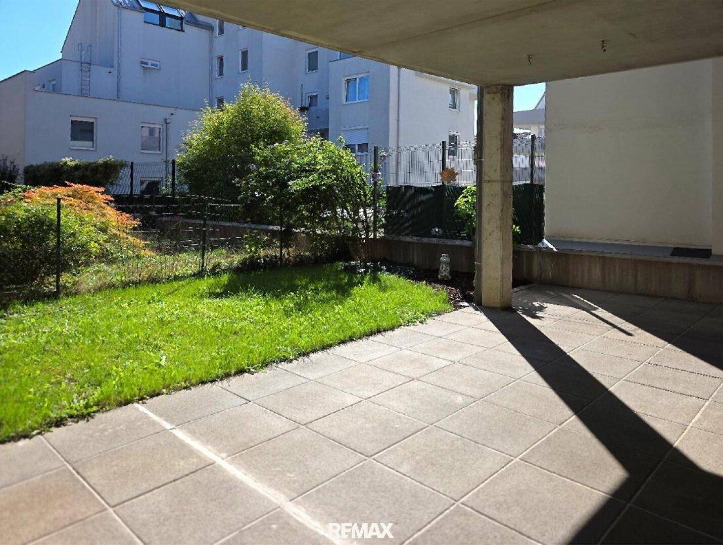 Sonniger Terrassenbereich mit Steinplatten und angrenzender kleiner Rasenfläche im Freien.