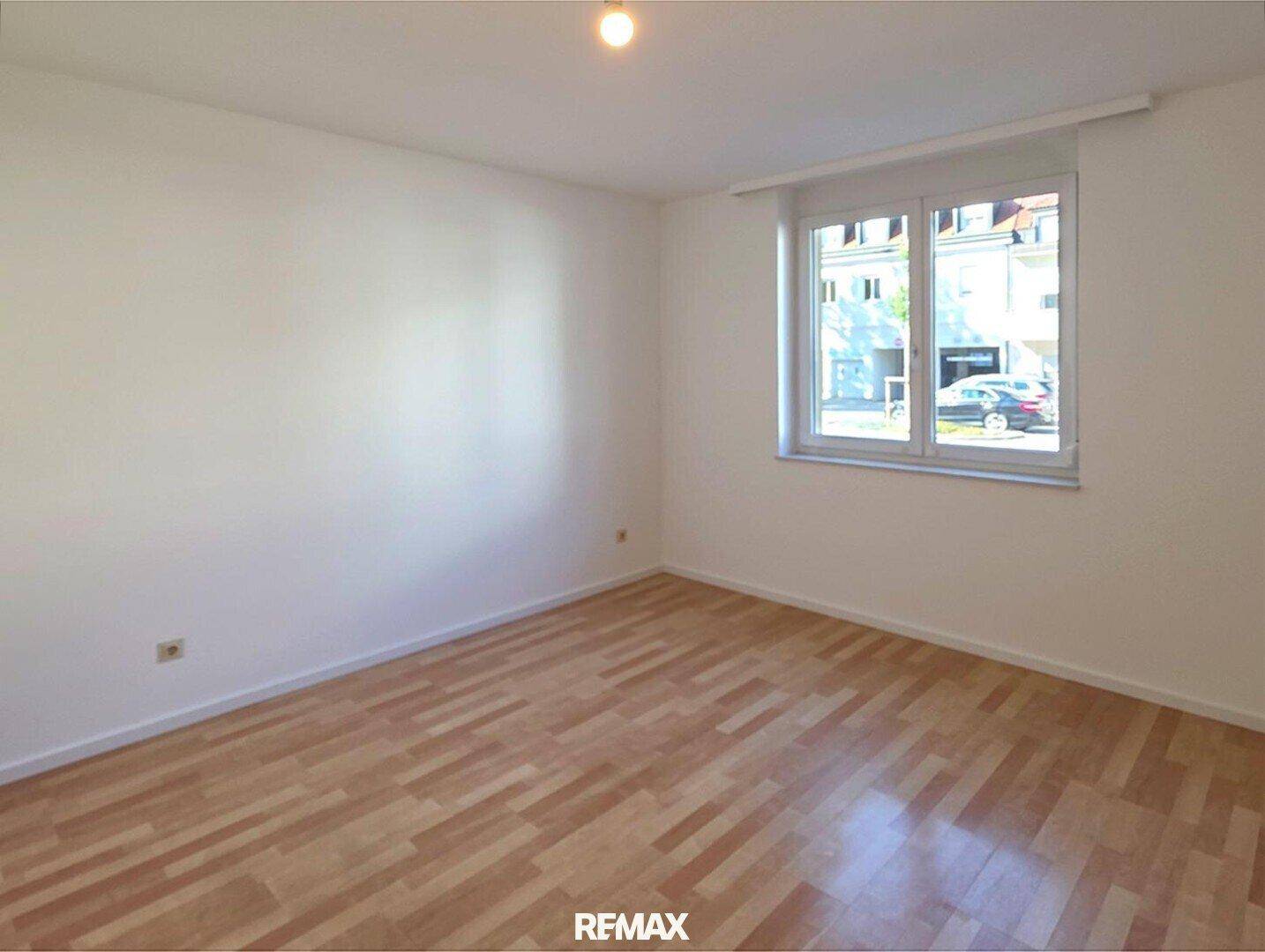 Leeres Zimmer mit Laminatboden und viel Tageslicht durch das große Fenster.