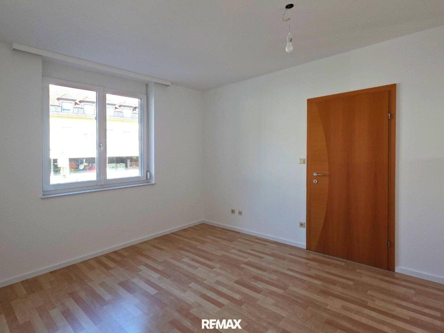 Helles Schlafzimmer mit Laminatboden und einem Fenster mit Blick nach draußen.