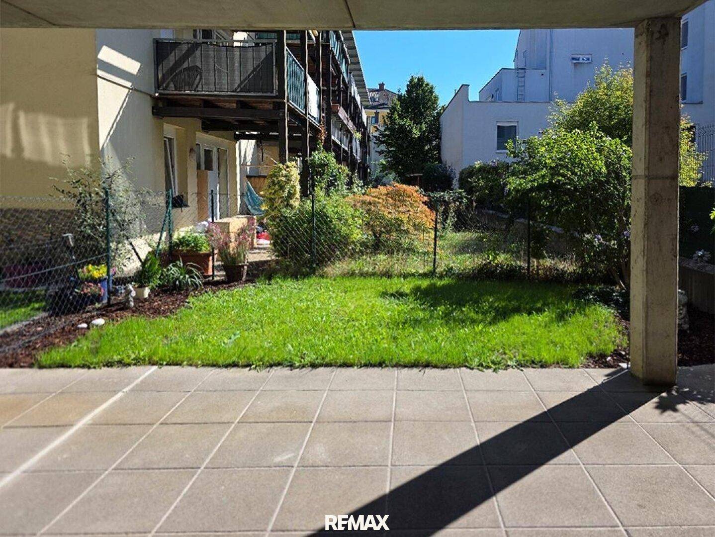Gepflasterte Terrasse mit Grünfläche und Blick auf die umliegenden Wohngebäude.
