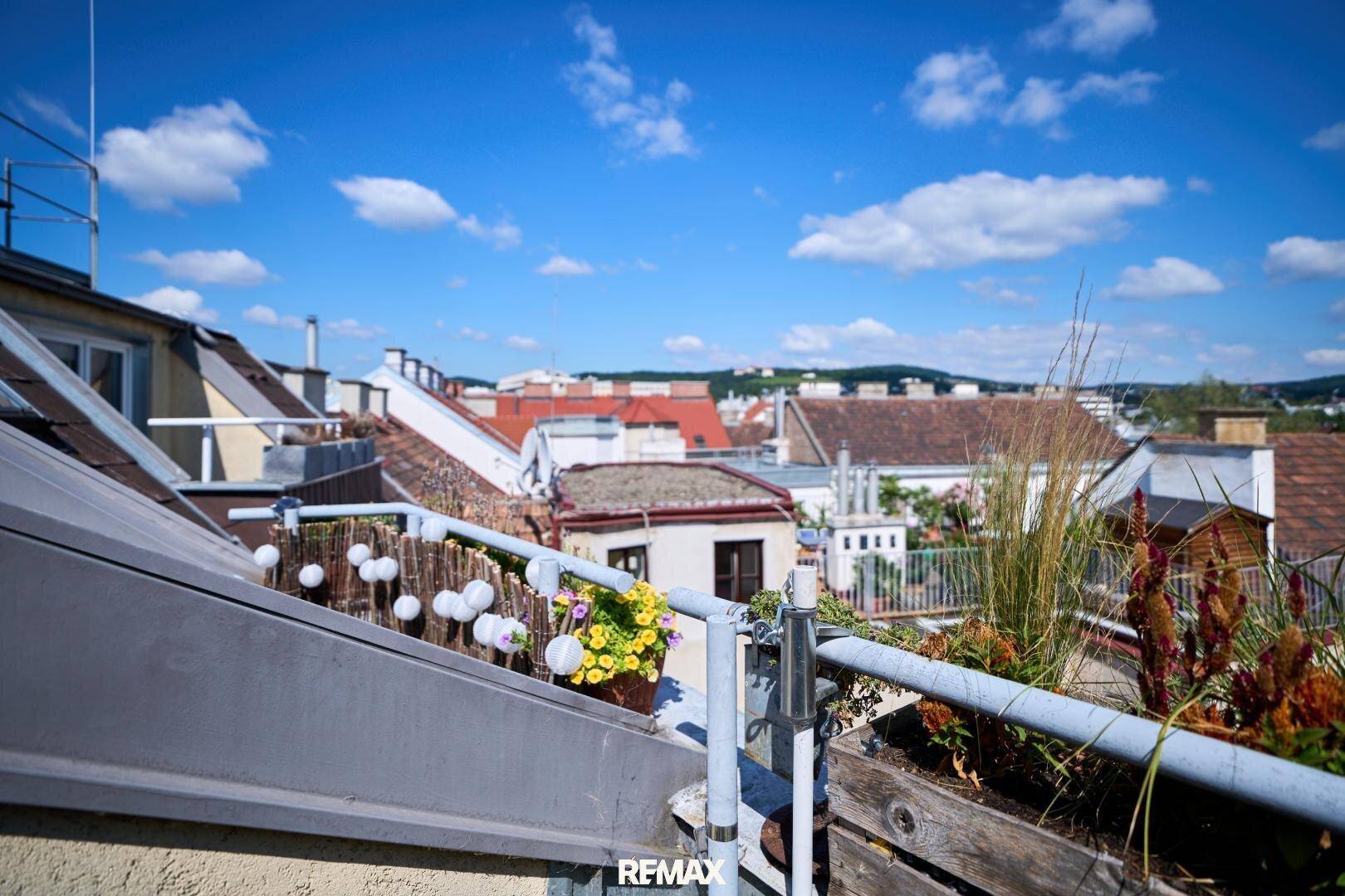 Weitblick über die Dächer der Stadt an einem sonnigen Tag mit dekorativen Pflanzen am Geländer.