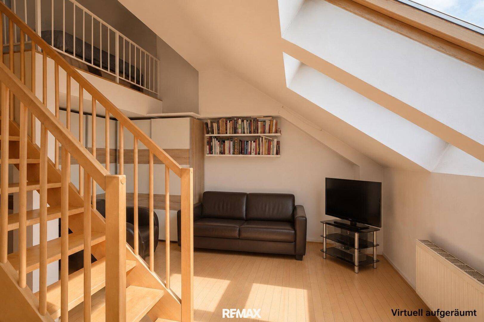 Gemütlicher Wohnbereich im Dachgeschoss mit Sofa, Fernseher und Holztreppe unter den Dachfenstern.