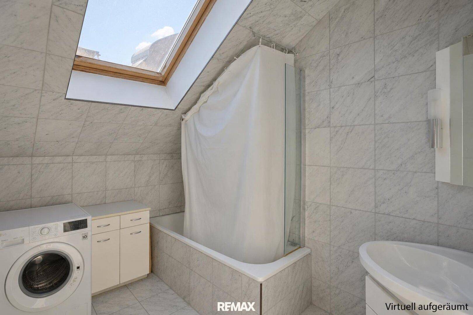 Badezimmer mit Badewanne, Waschmaschine und Dachfenster, komplett gefliest in hellem Marmor-Look.
