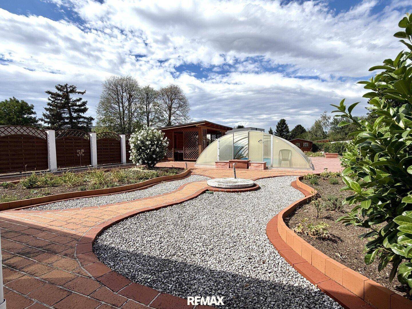 Weitläufiger Garten mit Poolabdeckung, gepflasterten Wegen und Gartenhaus unter bewölktem Himmel.