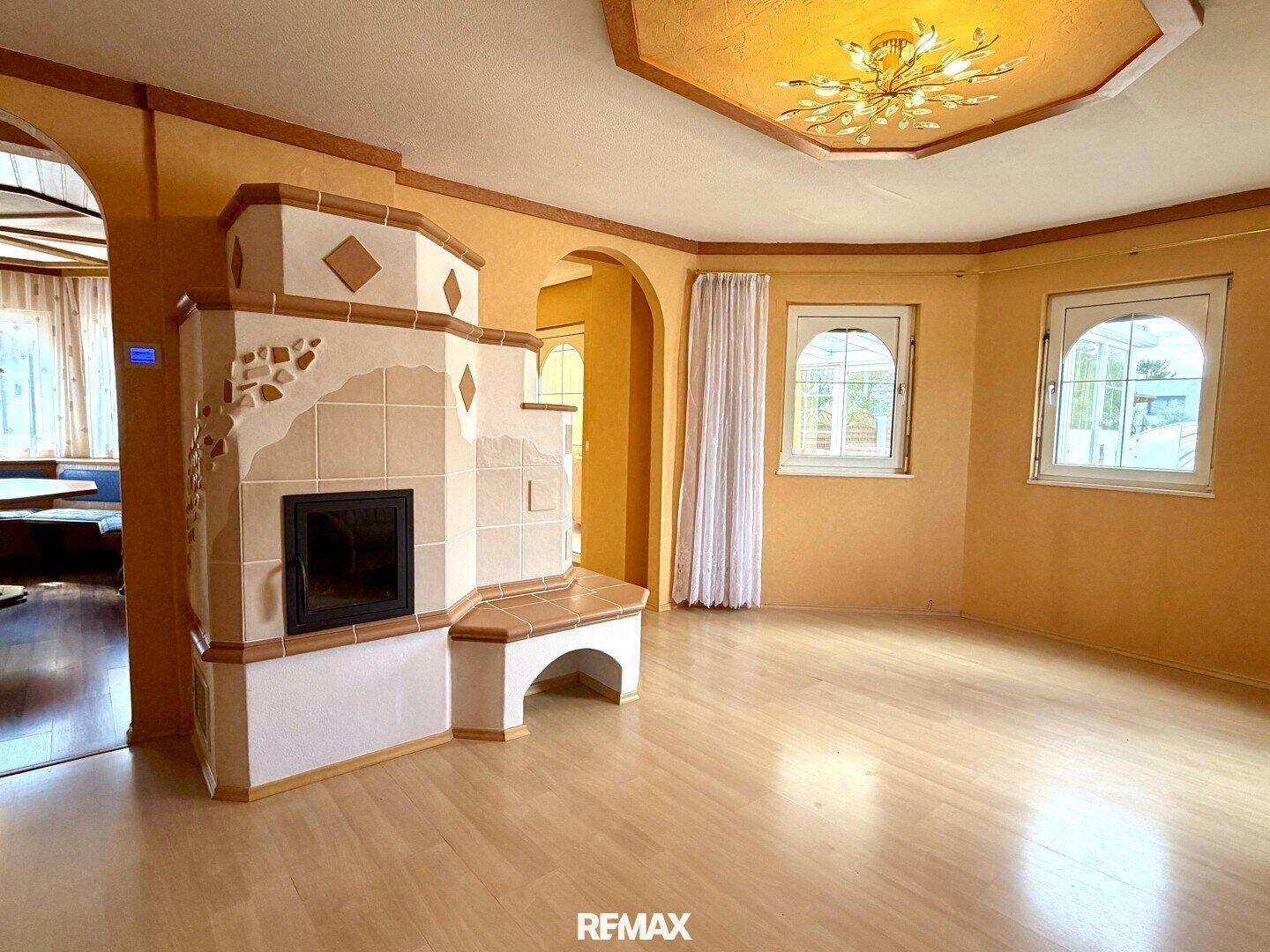 Geräumiges Wohnzimmer mit hellem Parkettboden und traditionellem Kachelofen als Blickfang.