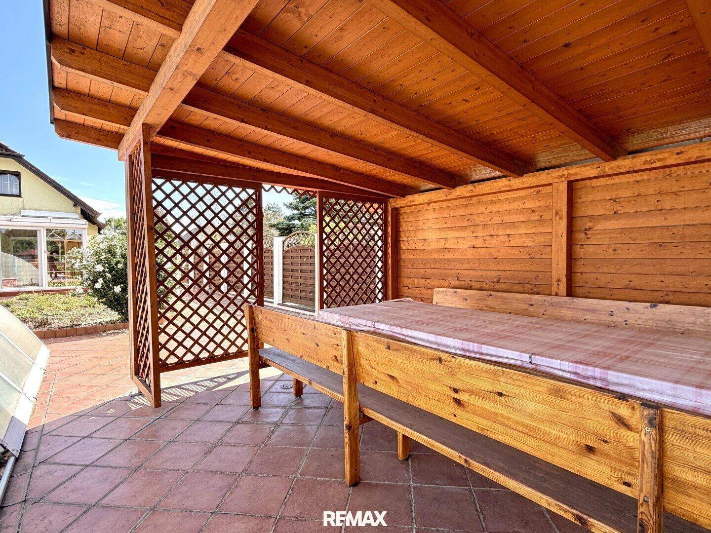 Überdachte Terrasse mit Holzbänken und Tisch, ideal für gesellige Stunden im Freien.