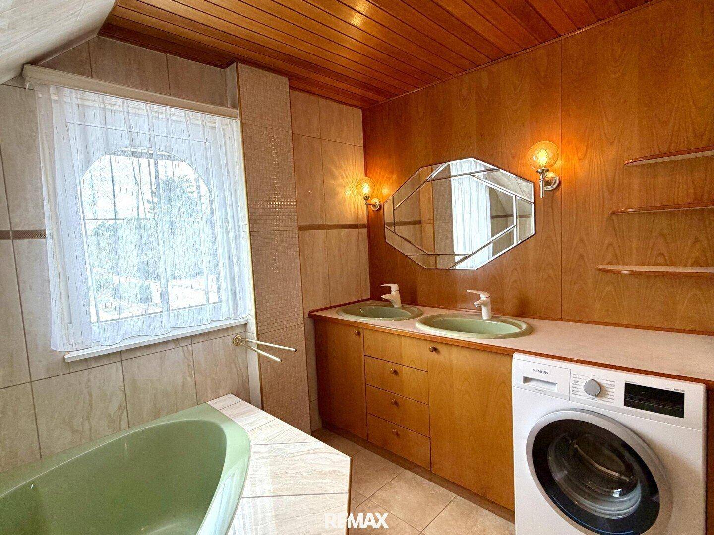 Badezimmer mit Doppelwaschbecken, Spiegelschrank und Waschmaschine unter Dachschräge.