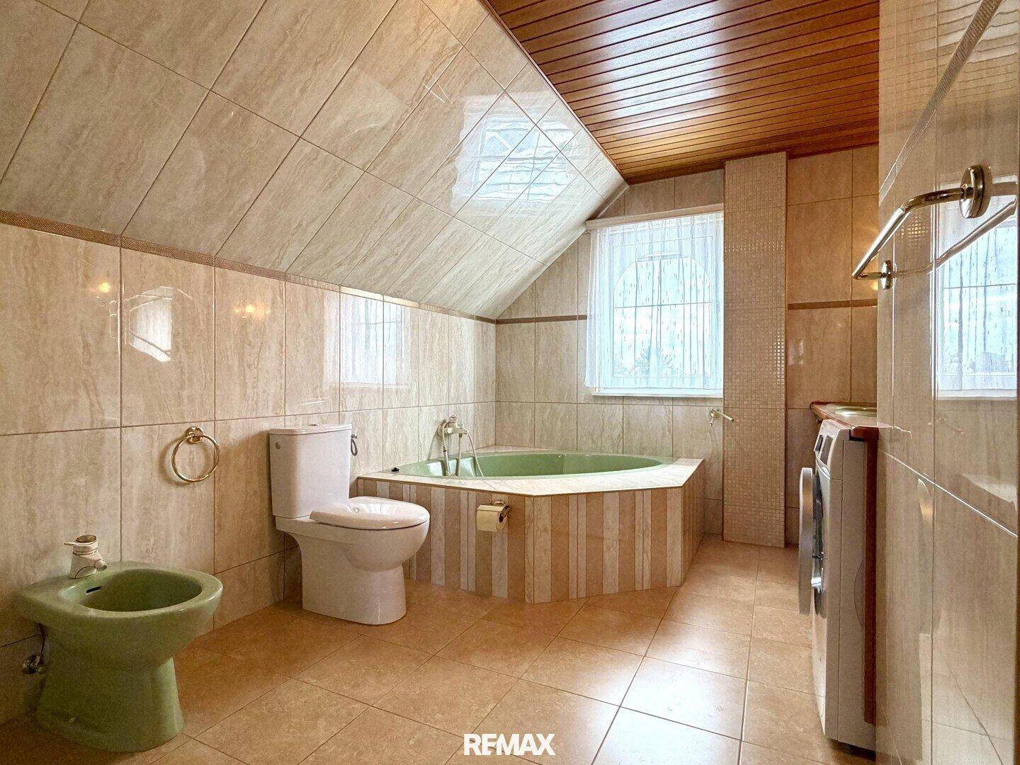 Geräumiges Badezimmer mit Eckbadewanne, Bidet und Fliesenboden unter Dachschräge.