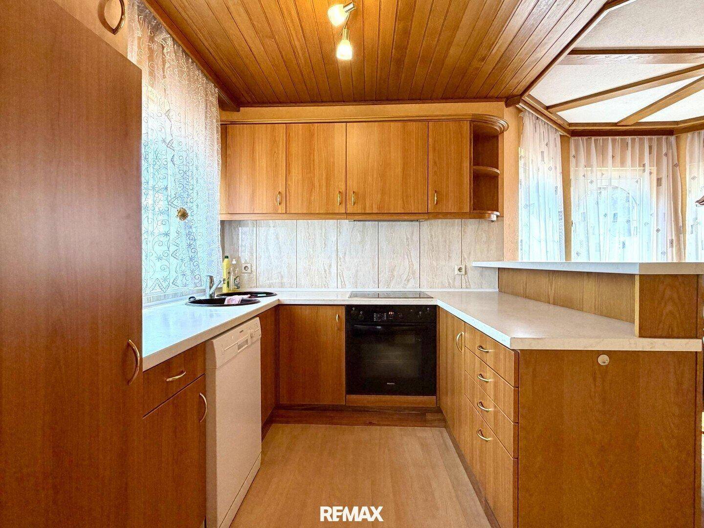 Funktionale Küche mit Holzschränken, Einbaugeräten und hellem Fliesenboden für den täglichen Gebrauch.