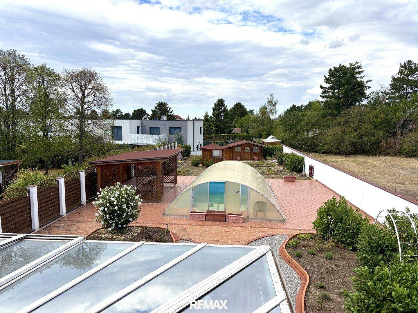 Weitläufiger Blick über den Garten mit Pool, Gartenhaus und Nachbargebäuden unter bewölktem Himmel.