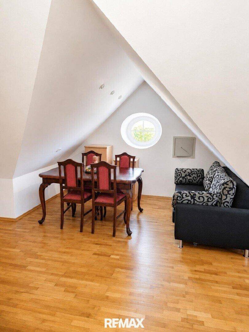 Gemütlicher Wohnbereich im Dachgeschoss mit Esstisch, Sofa und rundem Fenster.
