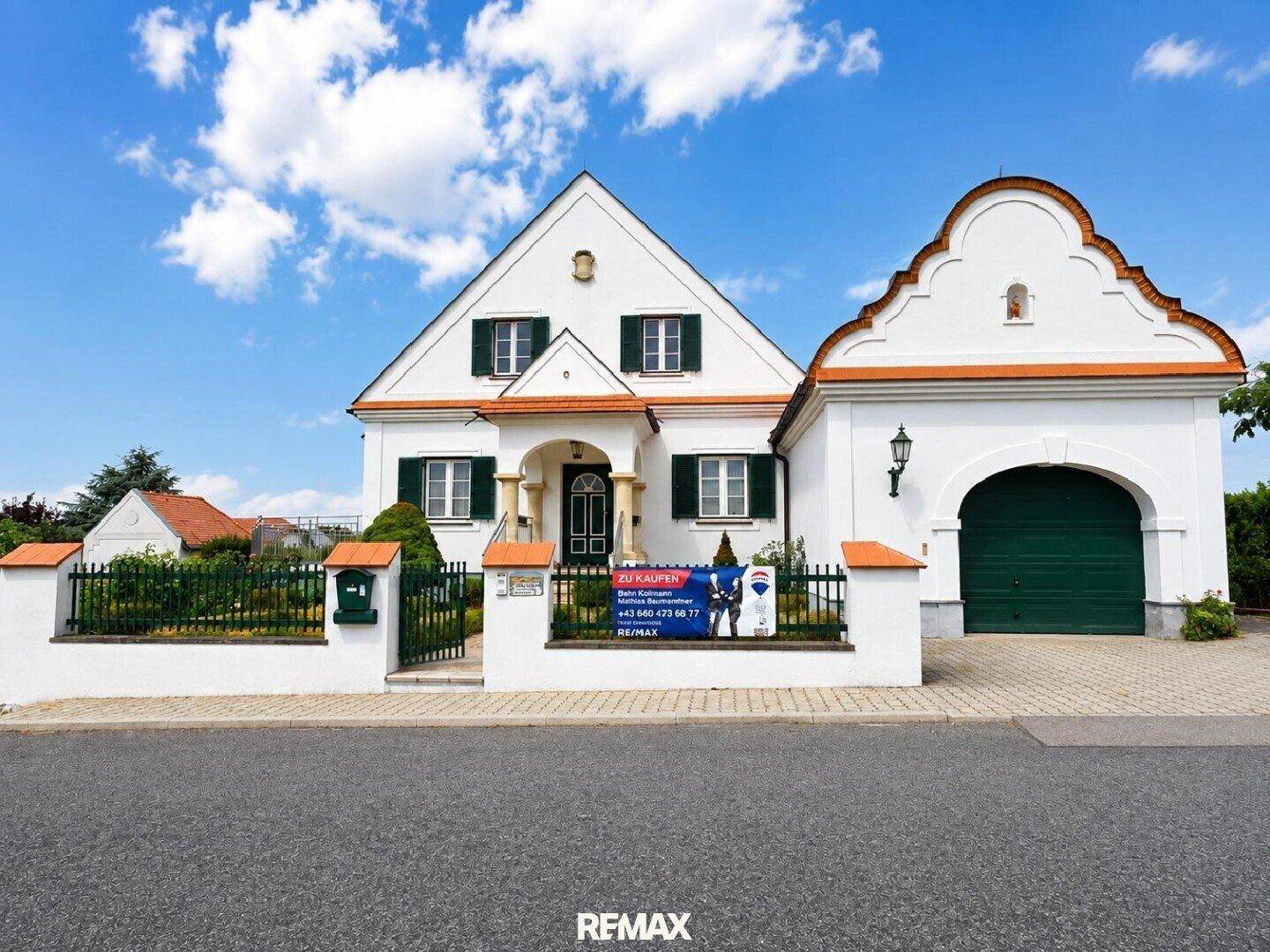 Vorderansicht des Hauses mit weißer Fassade, grünen Fensterläden und integrierter Garage.