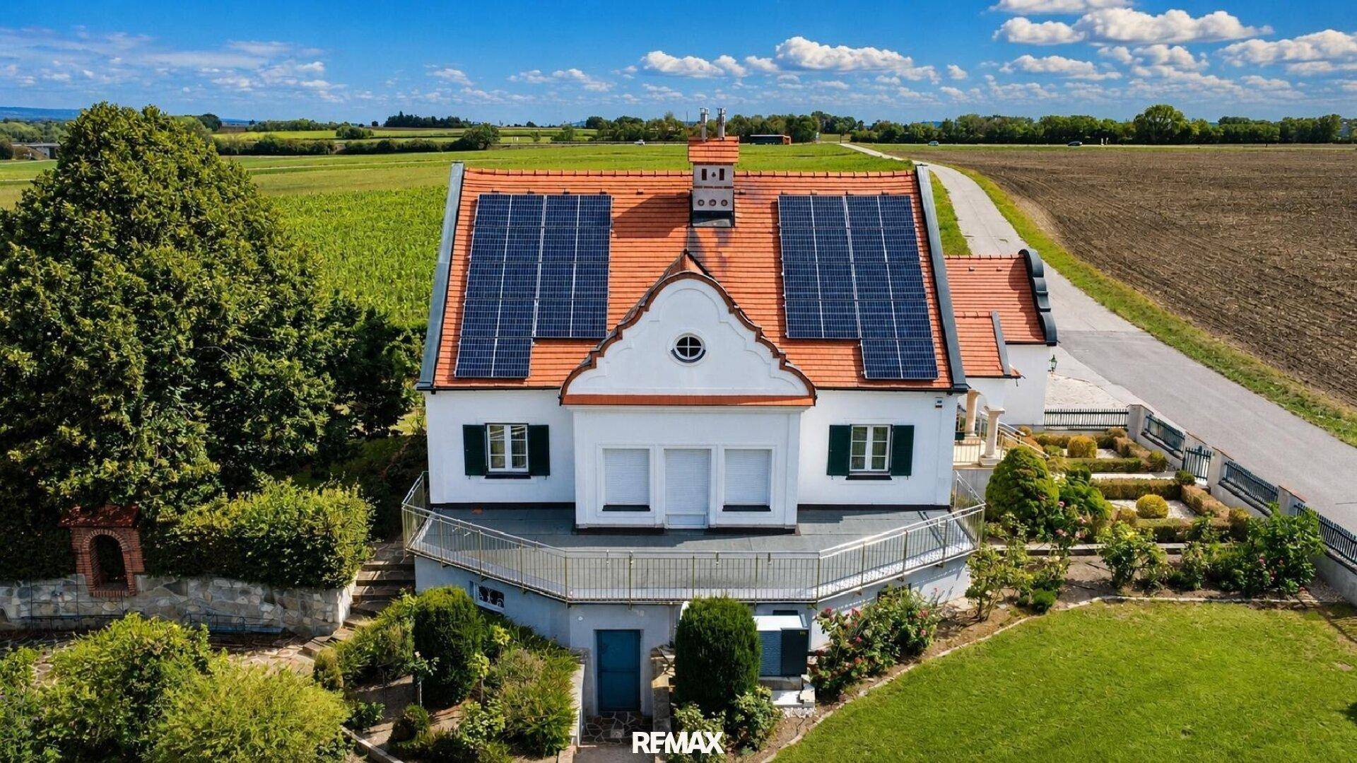 Haus mit Solaranlage auf dem Dach, umgeben von einem gepflegten Garten und Feldern.