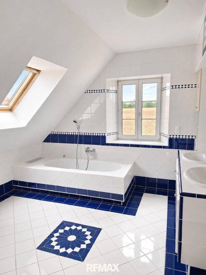 Helles Badezimmer mit blauen und weißen Fliesen, Badewanne und Dachfenster.