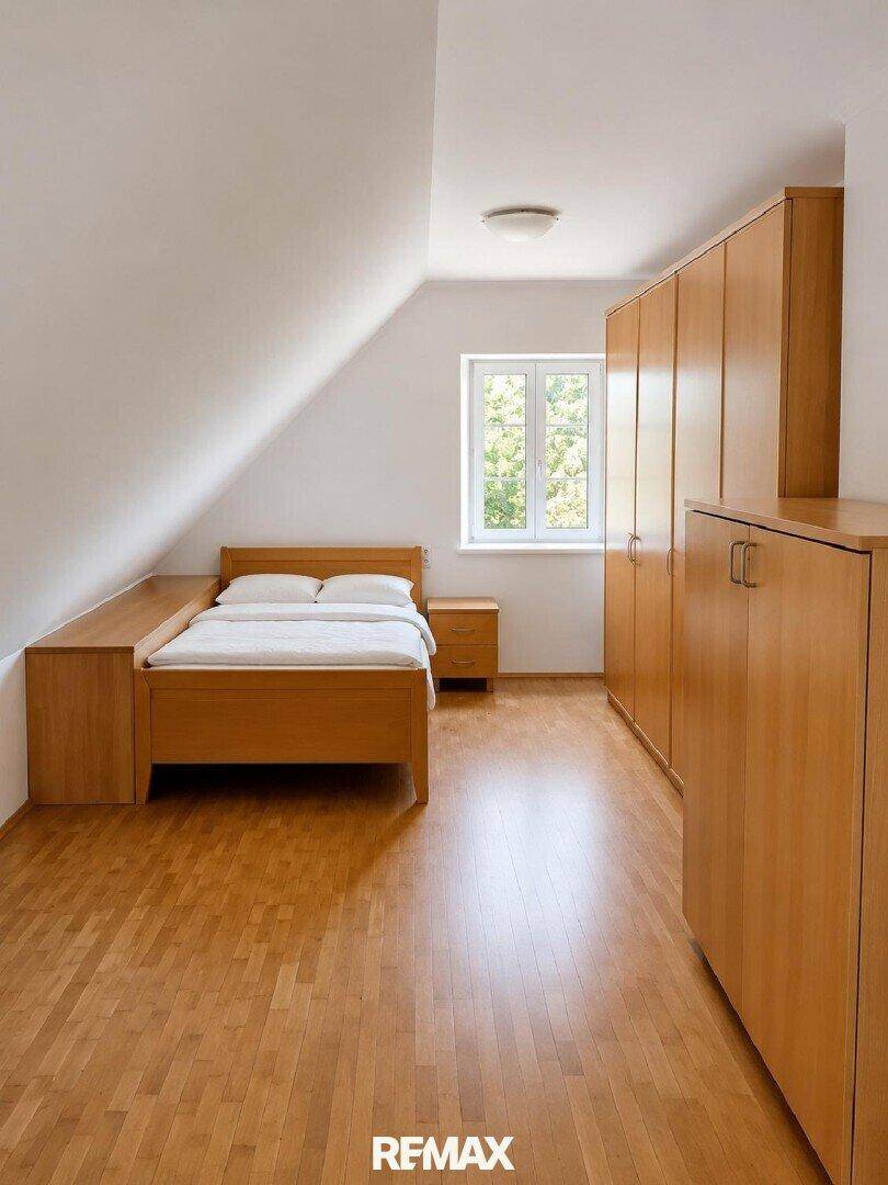 Helles Schlafzimmer im Dachgeschoss mit Holzmöbeln und schrägen Wänden.