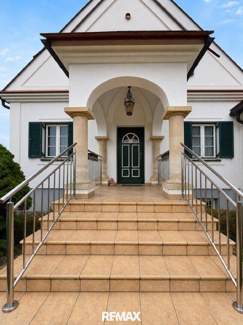Eingangsbereich des Hauses mit breiter Steintreppe, Säulen und einem eleganten Vordach.