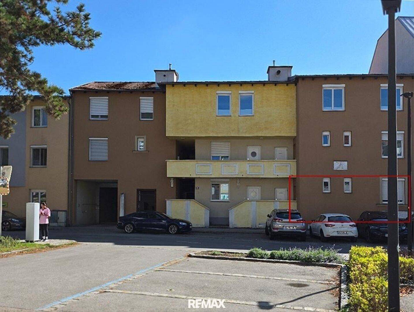 Mehrstöckiges Wohngebäude mit Parkplätzen davor und einer markierten Fassadenpartie.
