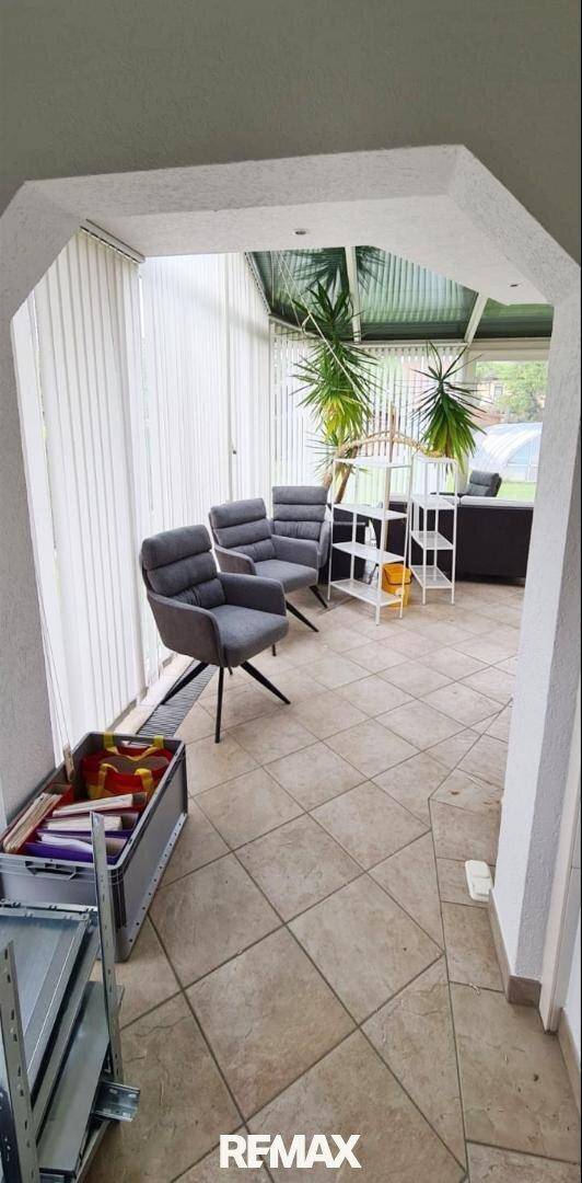 Heller Wintergarten mit Sitzgelegenheiten und Fliesenboden, ideal zum Entspannen.