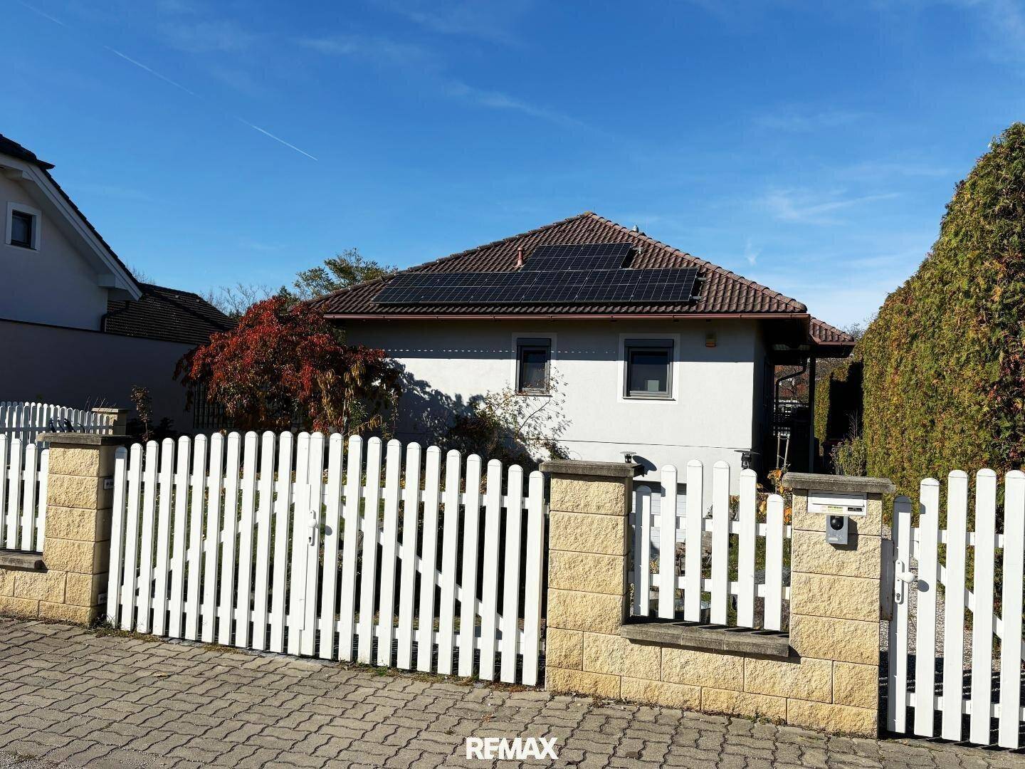 Vorderansicht des Hauses mit weißem Lattenzaun und Solarmodulen auf dem Ziegeldach.