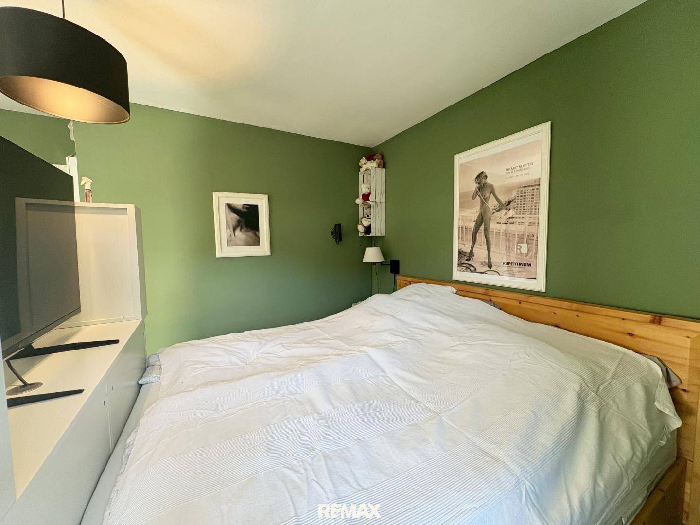 Schlafzimmer mit grünen Wänden, Holzbett und Laminatboden, gemütlich eingerichtet.