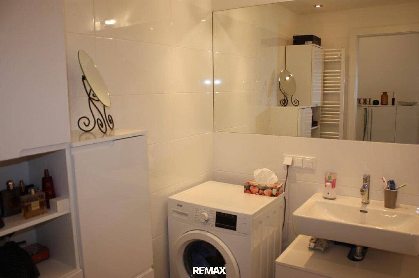 Modernes Badezimmer mit weißen Fliesen, Einzelwaschbecken und integrierter Waschmaschine.