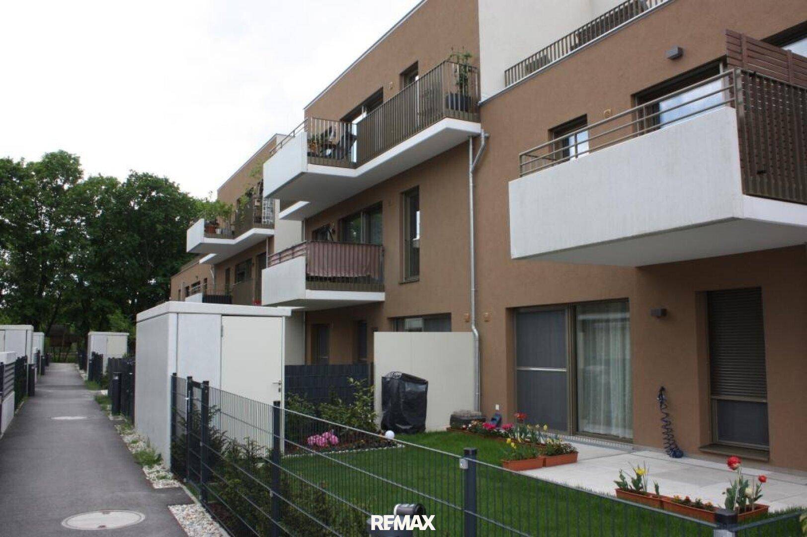 Moderne Wohnanlage mit brauner Fassade, Balkonen und privaten Gärten im Erdgeschoss.