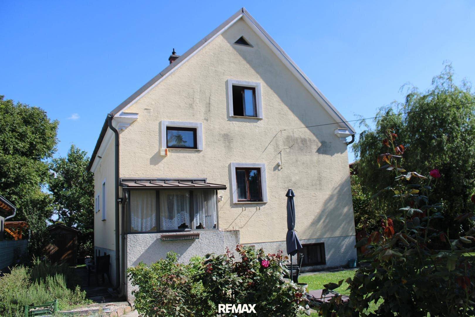 Hausrückseite mit gepflegtem Garten, Rosenbüschen und einem kleinen Sitzbereich im Freien.