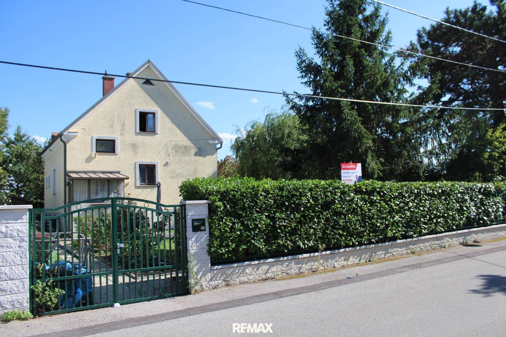 Vorderansicht des Hauses von der Straße aus, mit schmiedeeisernem Tor und hoher Hecke.