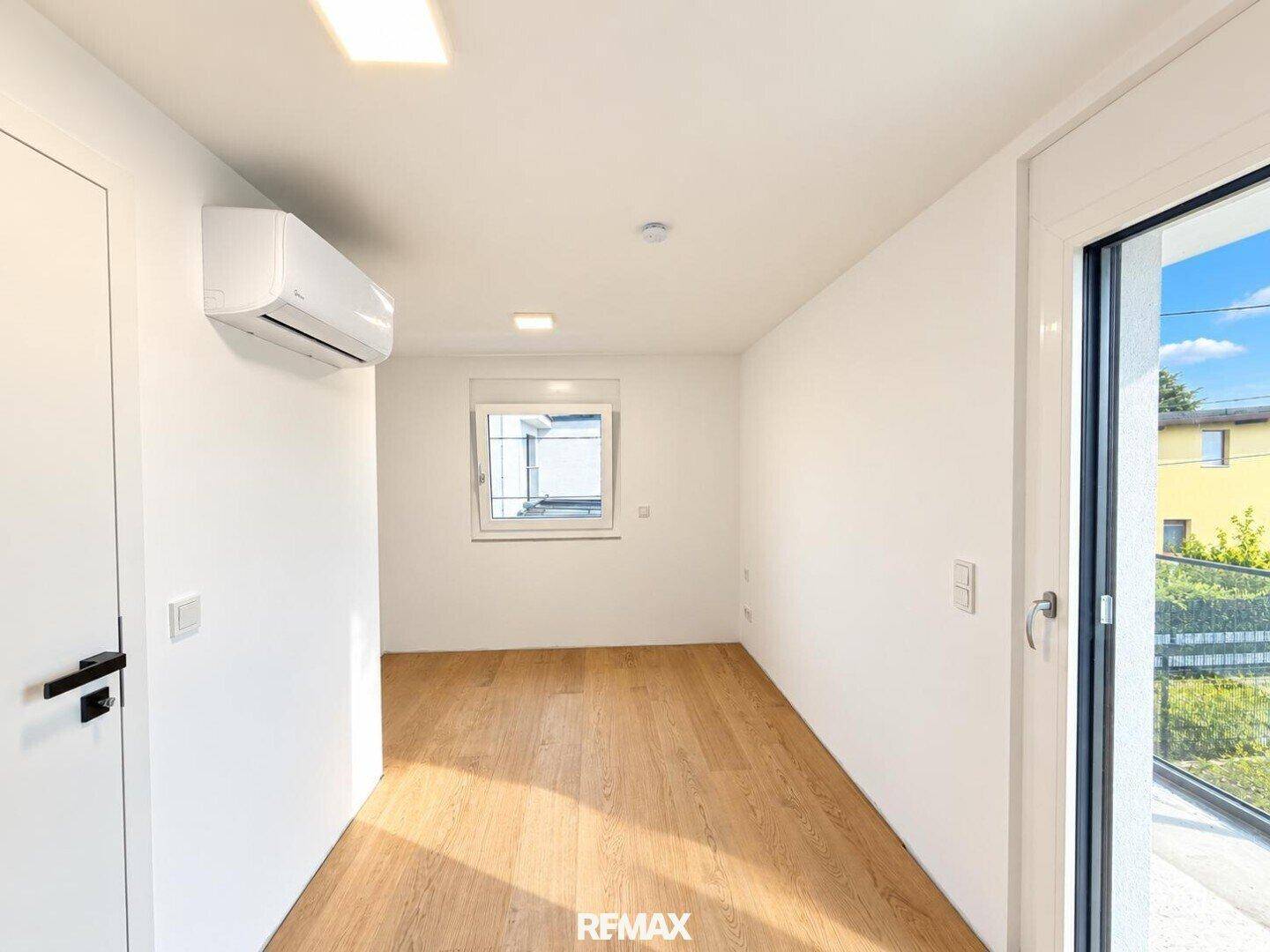 Helles, leeres Zimmer mit Holzboden und Balkontür, ideal für Schlaf- oder Arbeitszimmer.