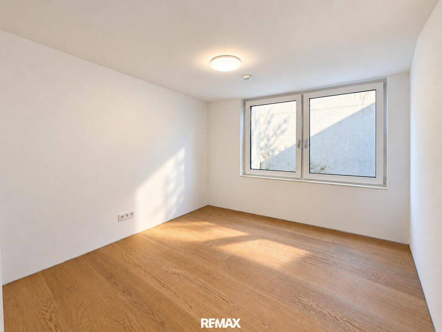 Helles, leeres Zimmer mit Holzboden und Fenster, ideal als Gäste- oder Arbeitszimmer.