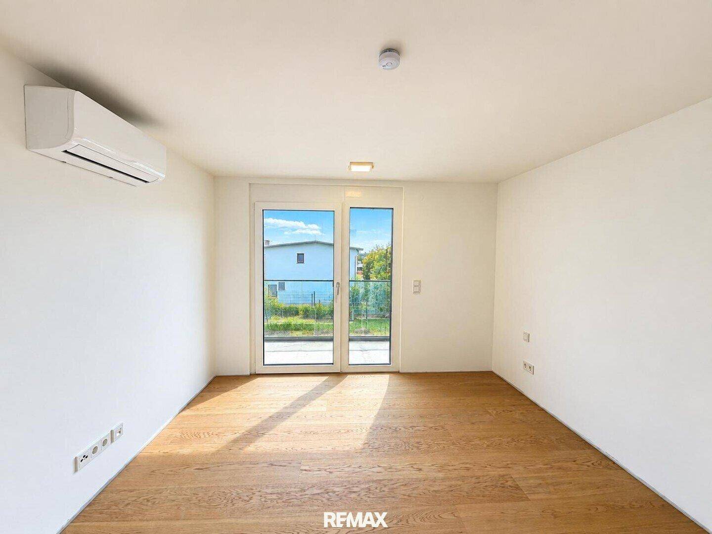 Helles, leeres Schlafzimmer mit Holzboden und Balkontür, bereit zur individuellen Gestaltung.