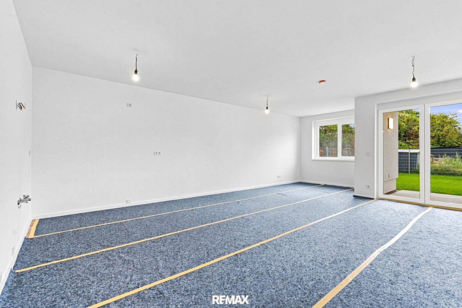 Geräumiger Wohnbereich mit großen Schiebetüren zum Garten und vorbereitetem Bodenbelag.