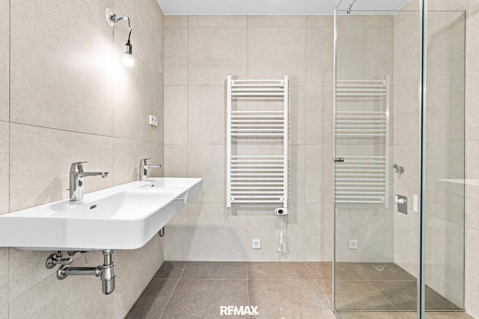 Modernes Badezimmer mit Doppelwaschbecken, begehbarer Dusche und beheiztem Handtuchheizkörper.