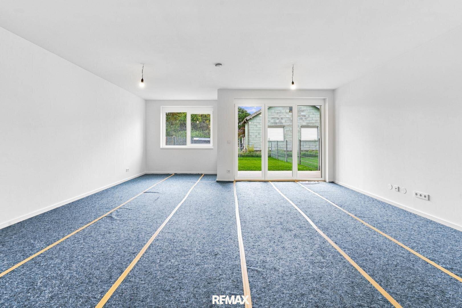 Heller Wohnraum mit großen Fensterfronten und direktem Zugang zur Grünfläche im Freien.