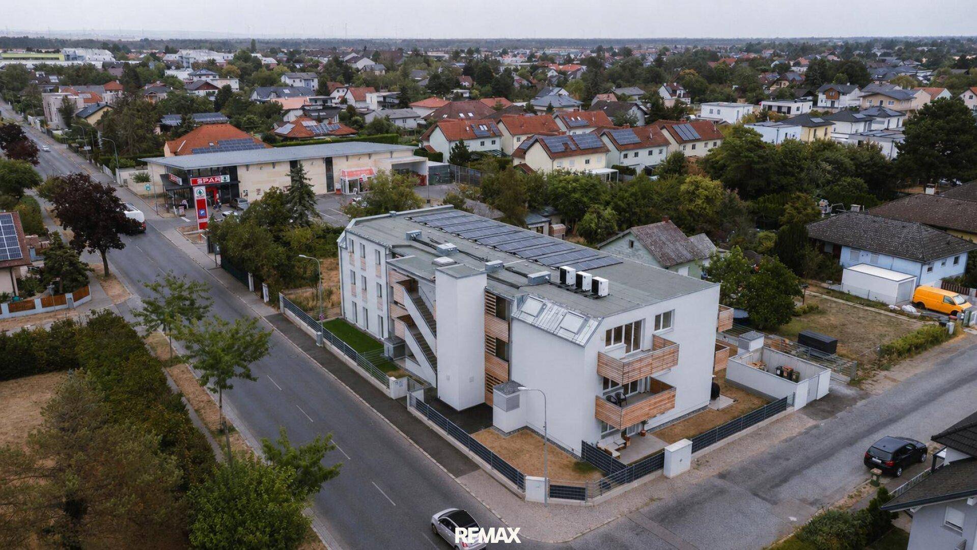 Luftaufnahme eines modernen Mehrfamilienhauses mit Solaranlage auf dem Dach in Wohngegend.