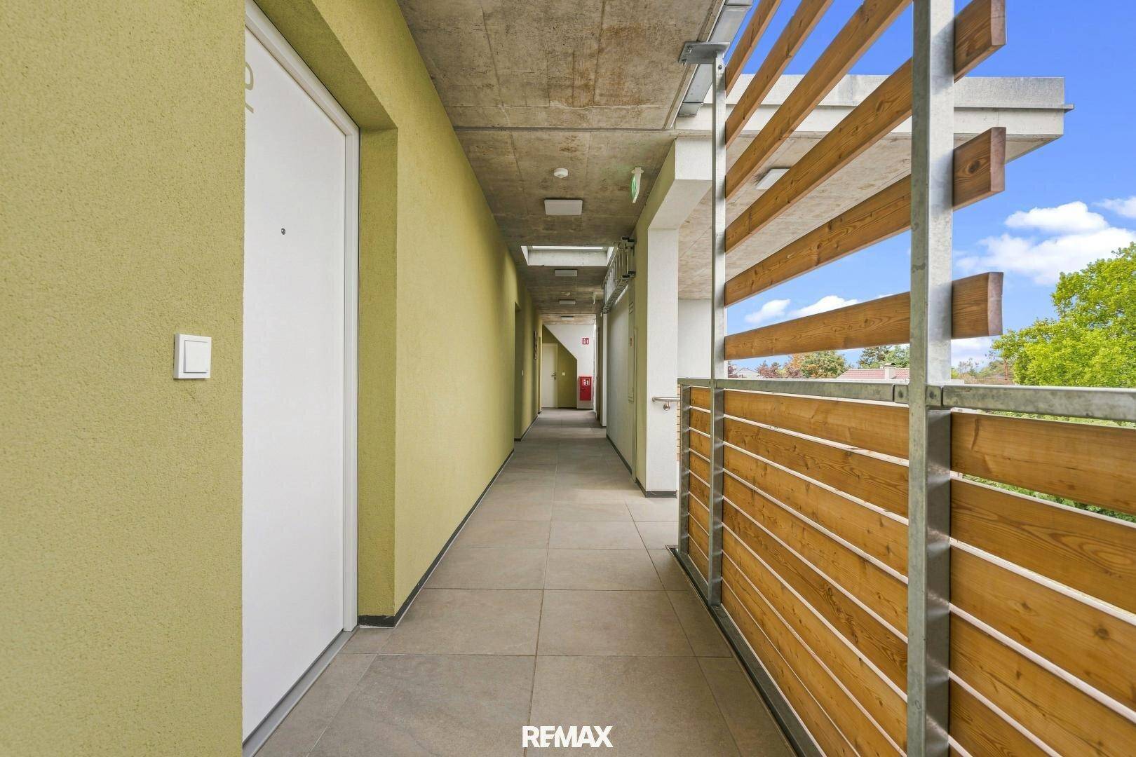 Langer Außenflur mit Holzelementen und Blick ins Freie, der zu den Wohneinheiten führt.
