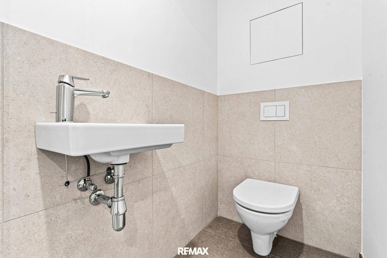 Modernes Gäste-WC mit wandhängender Toilette und kleinem Waschbecken in hellen Fliesen.