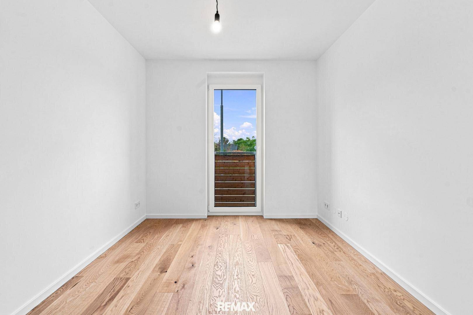 Helles, unmöbliertes Zimmer mit Holzboden und großem Fenster für viel Tageslicht.