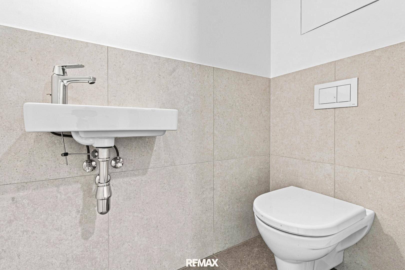 Modernes Gäste-WC mit Wand-WC und kleinem Waschbecken, hell gefliest.