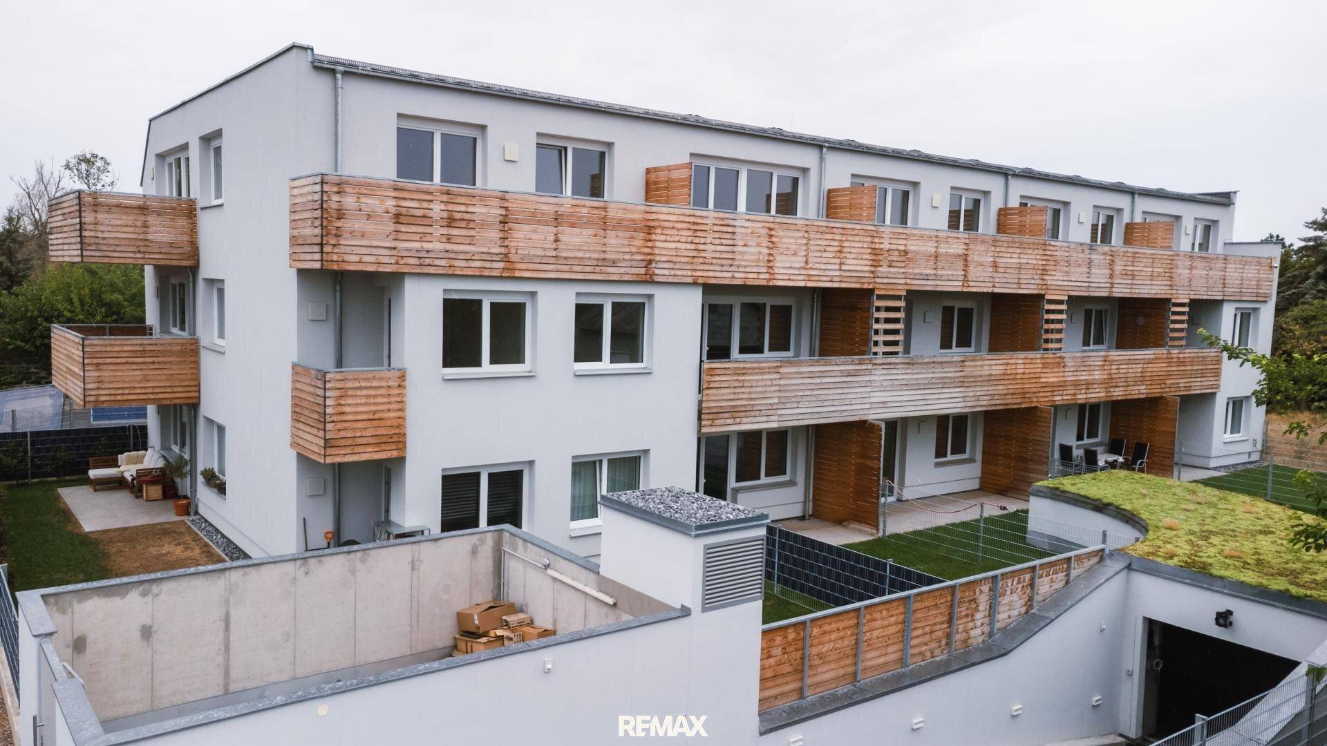 Ansicht der modernen Wohnanlage mit Balkonen, Gärten und Zugang zur Tiefgarage.