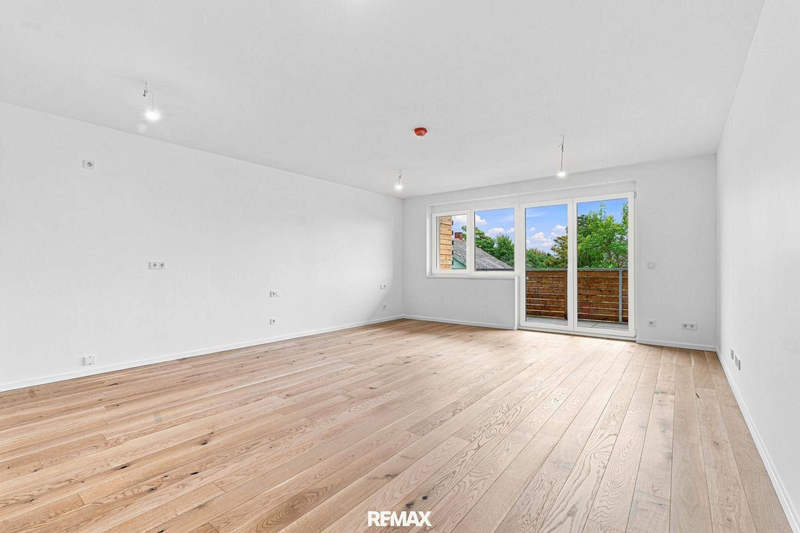 Heller, leerer Raum mit Holzboden und Zugang zu einem Balkon, ideal für einen Wohnbereich.