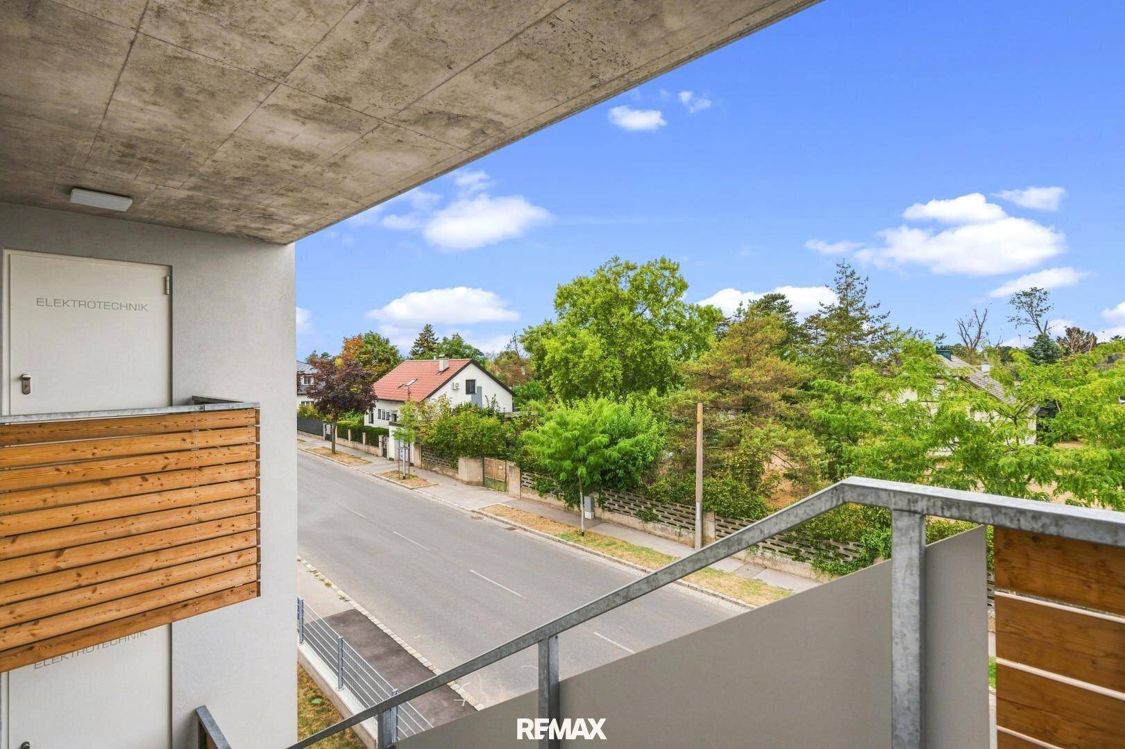 Blick vom Balkon auf die grüne Umgebung und die Straße mit Häusern.