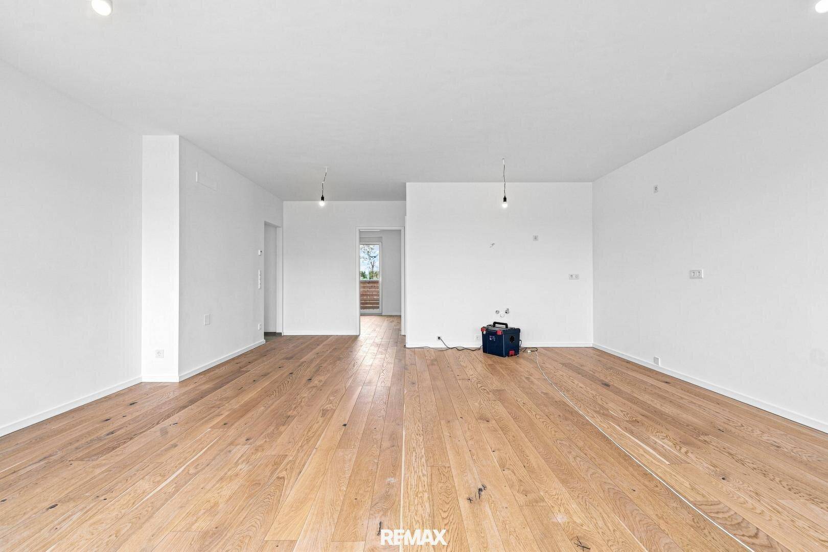 Unmöblierter Wohnraum mit Holzboden und offenem Zugang zu weiteren Zimmern im Neubau.
