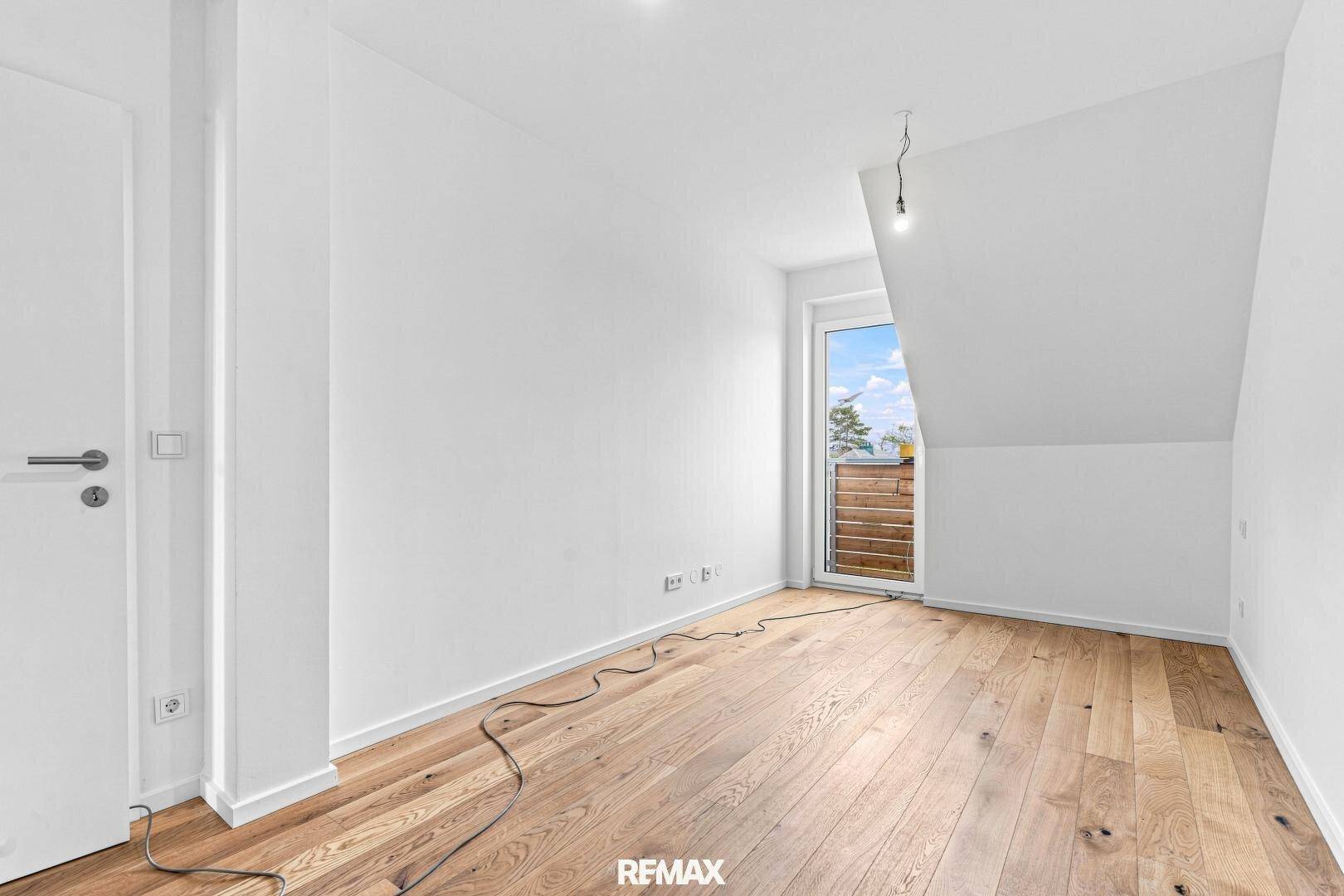 Helles Schlafzimmer mit Dachschräge, Holzboden und Zugang zu einem kleinen Balkon.