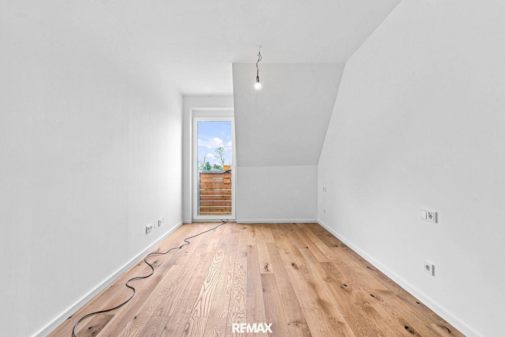Unmöbliertes Zimmer mit Holzboden, Dachschräge und Tür zum Außenbereich, ideal als Schlafzimmer.