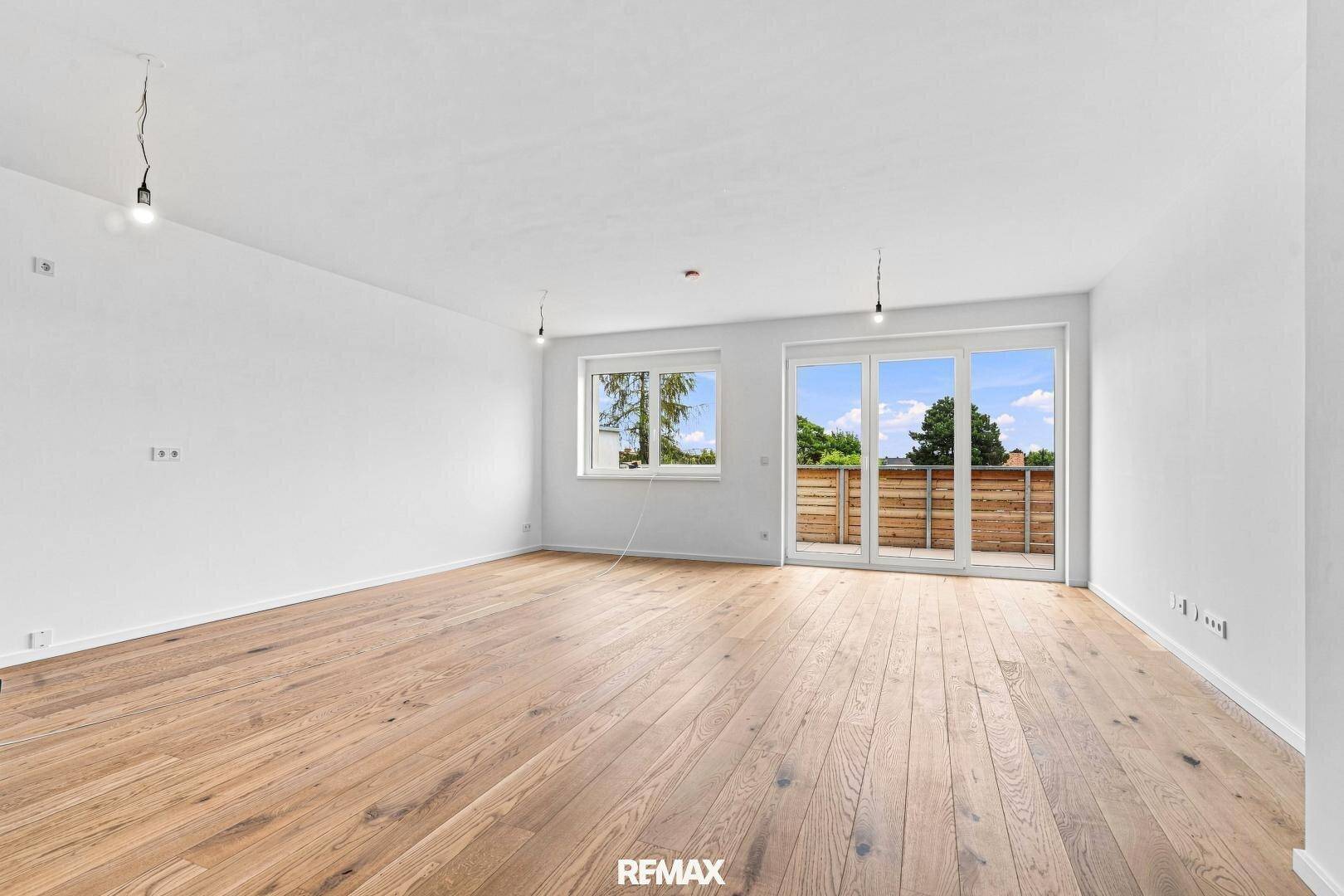 Geräumiger, unmöblierter Wohnbereich mit hellem Holzboden und Zugang zu einem Balkon.