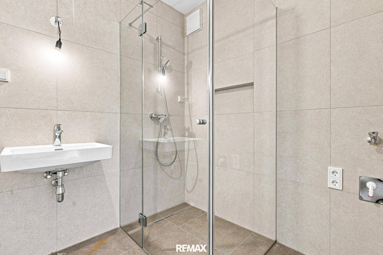 Modernes Badezimmer mit begehbarer Dusche, Waschbecken und hellen Fliesen, funktional und stilvoll gestaltet.