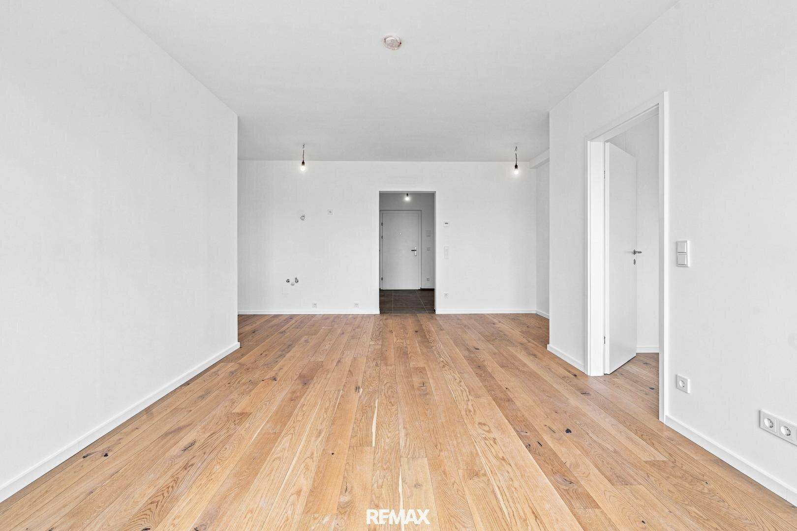 Geräumiges, leeres Wohnzimmer mit Holzboden und Zugang zu weiteren Räumen, bereit zur Gestaltung.