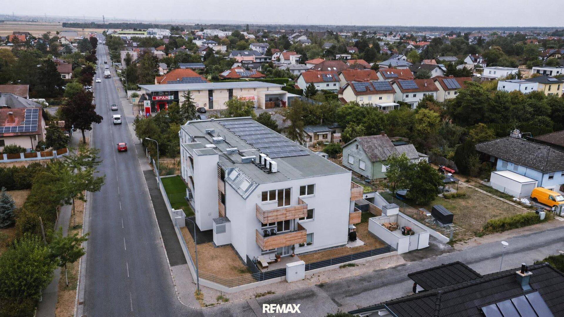Luftaufnahme eines modernen Wohngebäudes an einer Straße mit umliegender Bebauung und viel Grün.